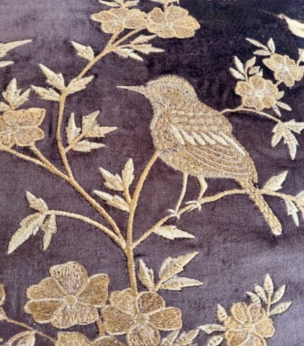 Zoom in einen dunkelbraunen Kissenbezug aus Samt mit goldenen Applikationen eines Spatzes und Ästen