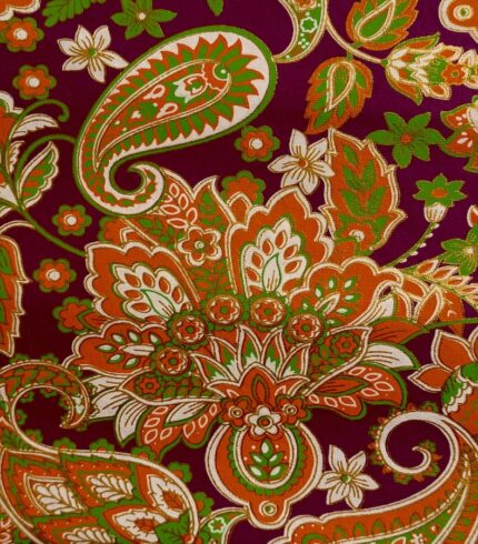 Zoom in ein handbedrucktes, dunkelviolettes Papiers mit kräftigen orangefarbenen Blütenornamenten unterbrochen von grasgrünen und weissen Blütenblättern