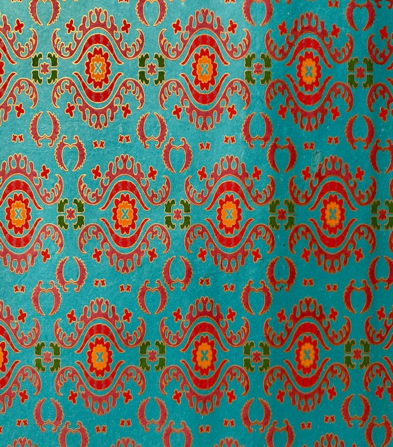 P015_1 Frontalansicht eines handbedruckten, blautürkisen Papiers mit kräftigen rotorangenen Ornamenten unterbrochen von olivgrünen und pinken Ornamenten