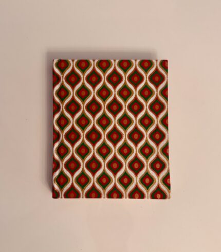 Frontalansicht eines handgefertigten Notizbuches mit grün-rotem, tropfenförmigen Design in Gold umrandet.