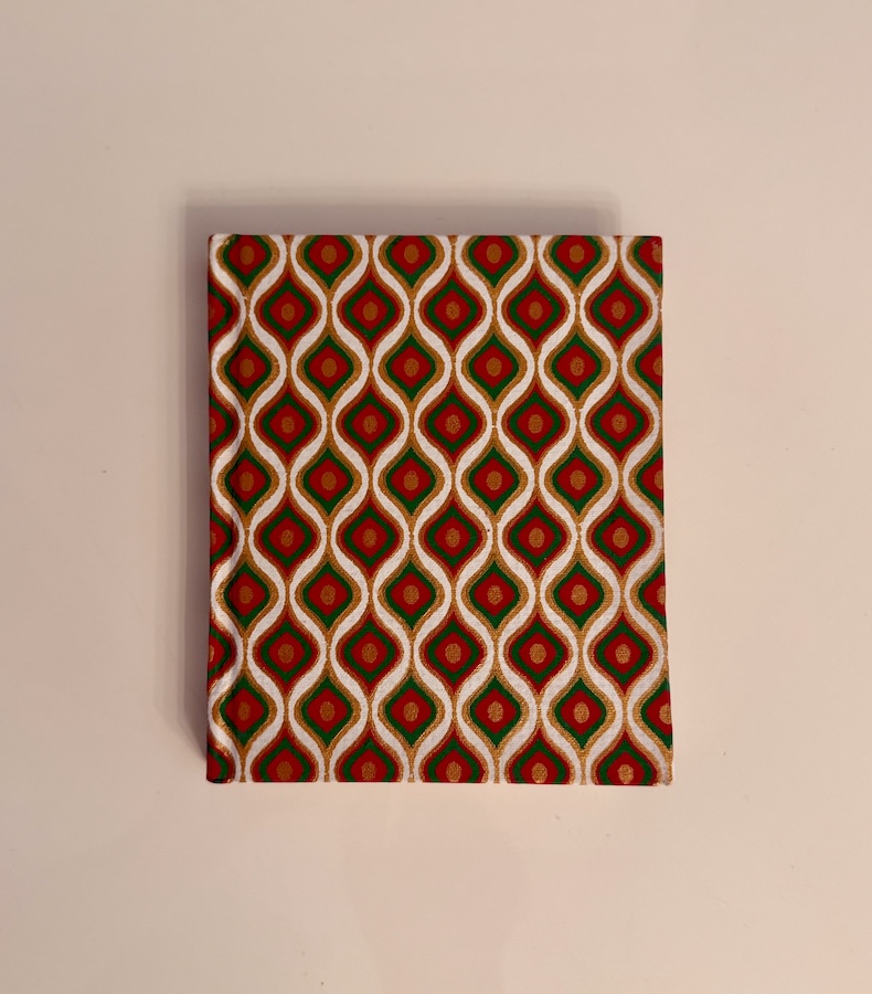P020_1 Frontalansicht eines handgefertigten Notizbuches mit grün-rotem, tropfenförmigen Design in Gold umrandet.