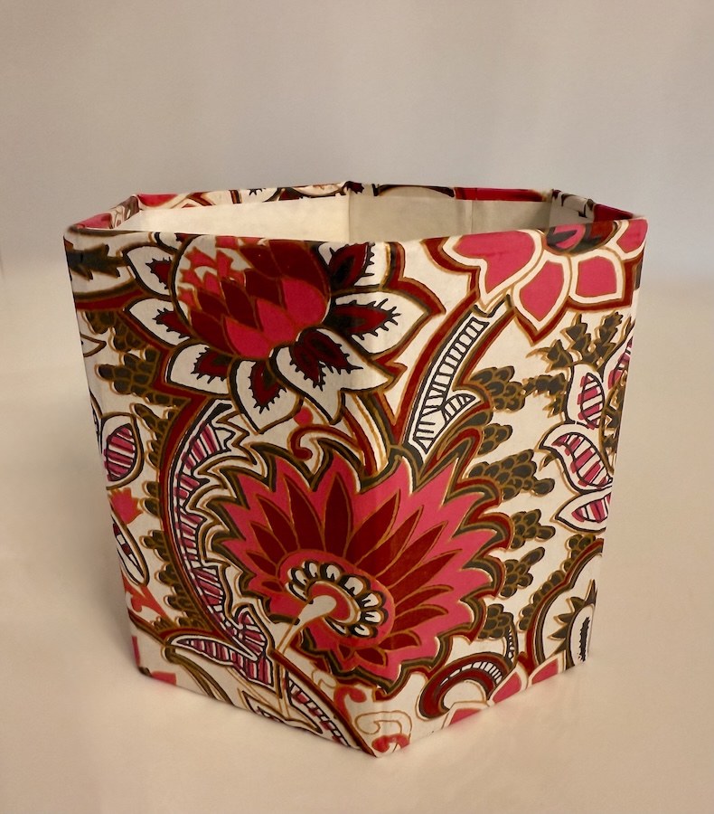 P021_1 Frontalansicht eines sechseckigen, handbedruckten, cremefarbenen Papierständers mit kräftigen rosafarbenen Blütenornamenten