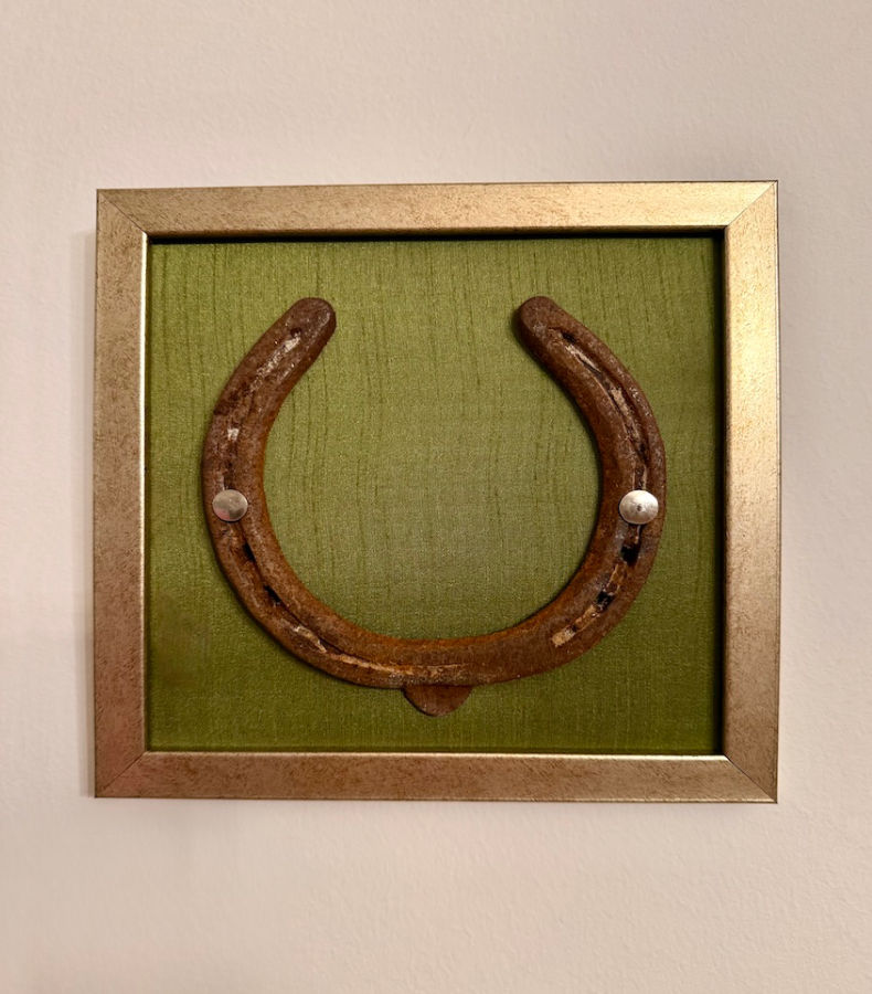 W009_1_v2 Frontalansicht auf ein Kunstwerk auf olivgrüner Seide mit einem antiken Hufeisen mittig platziert