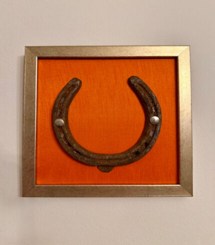 Frontalansicht auf ein Kunstwerk auf orangener Seide mit einem antiken Hufeisen mittig platziert