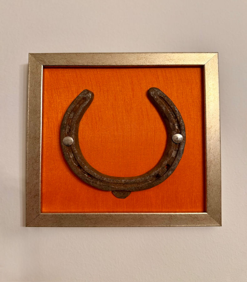 W010_1_v2 Frontalansicht auf ein Kunstwerk auf orangener Seide mit einem antiken Hufeisen mittig platziert