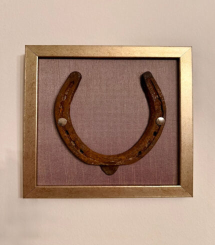 Frontalansicht eines Kunstwerk auf lavendelfarbener Seide mit einem antiken Hufeisen mittig platziert