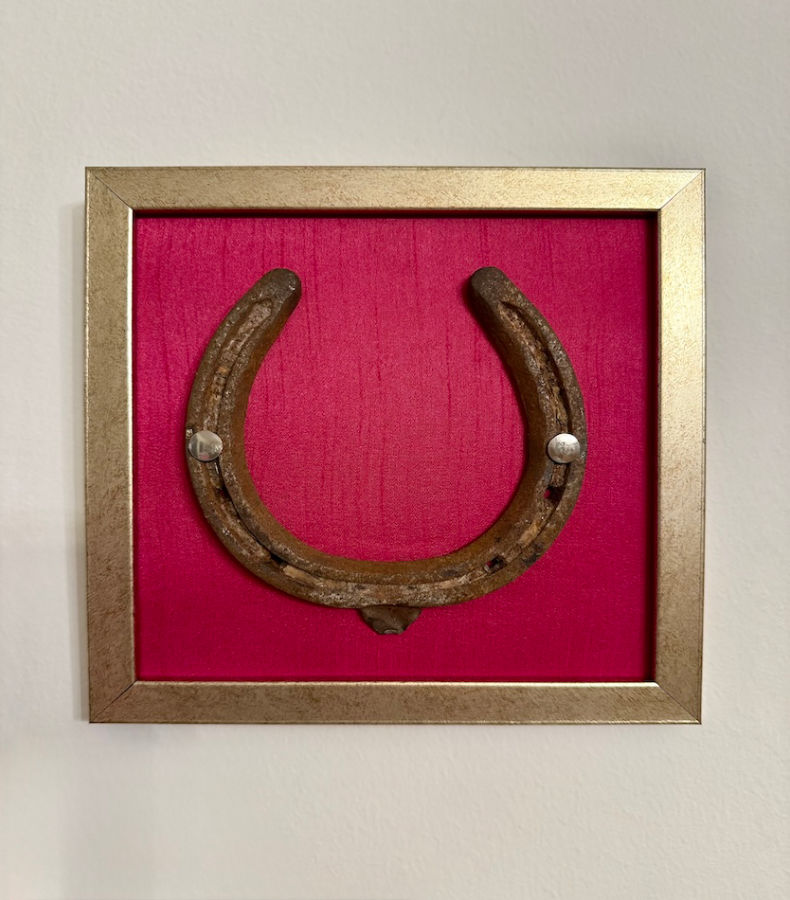 W014_1_v2 Frontalansicht eines Kunstwerk auf magentafarbener Seide mit einem antiken Hufeisen mittig platziert