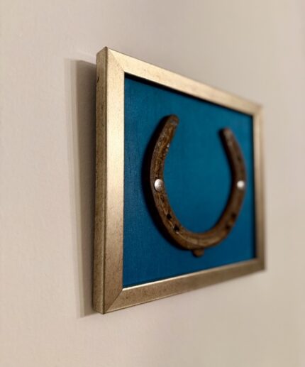 Seitenansicht eines Kunstwerk auf himmelblauer Seide mit einem antiken Hufeisen mittig platziert